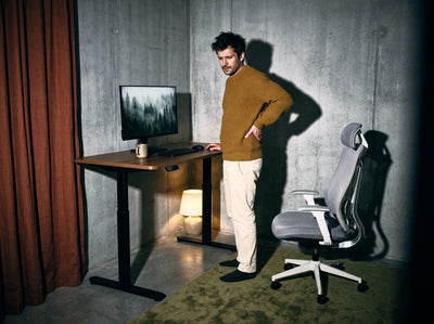 Mężczyzna stoi przy biurku i trzyma się za krzyż, obok fotel Ergonix OmniSit Pro